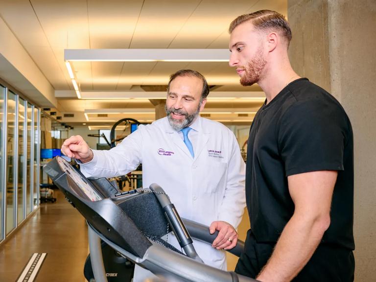 A male patient, right, uses exercise equipment while a male doctor, left, assists him.
