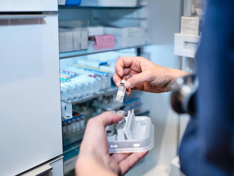 A healthcare worker takes a vial of liquid medication from a refrigerator shelf. stock photo.