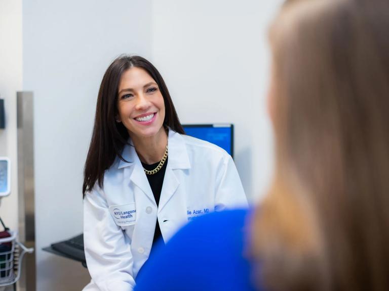 A female doctor sits and smiles while speaking with a patient.
