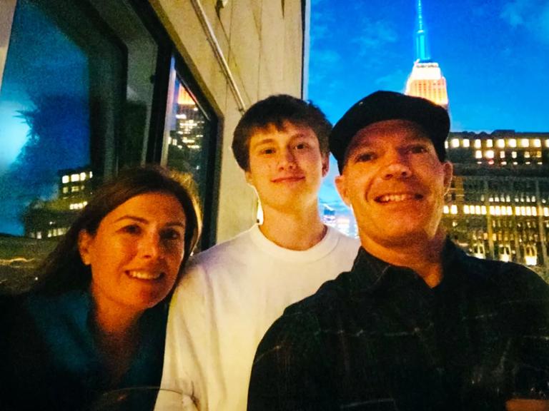 Logan standing with his mom and dad in front of the Empire State Building.