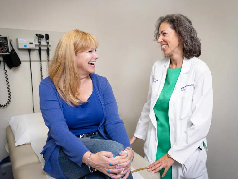 Harmony Reynolds, MD, talks with a smiling patient sitting on an exam table.