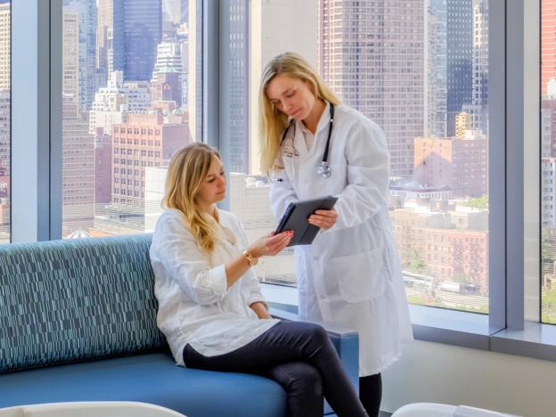 A doctor discusses medical care with a patient while looking at a tablet in a hospital room.