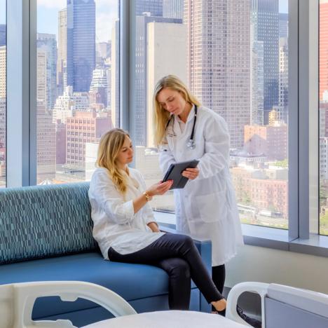 A doctor discusses medical care with a patient while looking at a tablet in a hospital room.