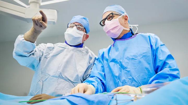 Mathew Williams, MD, and Cezar Staniloae, MD, both wearing surgical scrubs, stand at an operating room table during a procedure.