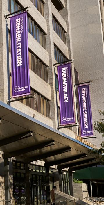 Three vertical purple signs hang on the exterior walls of NYU Langone Orthopedic Hospital.