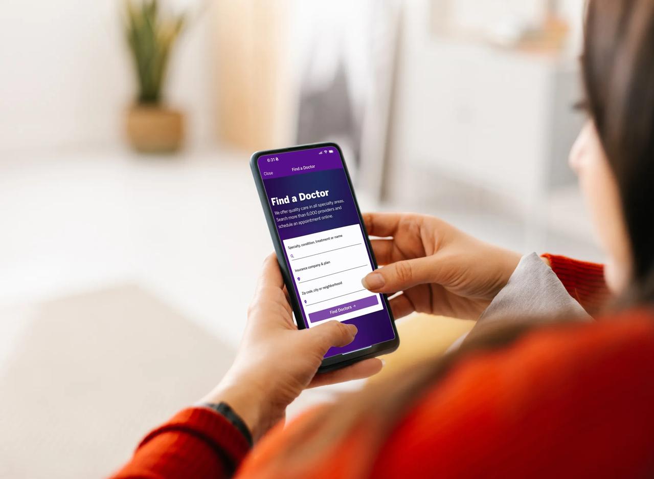 Photography of two hands holding their mobile phone, which displays the NYU Langone's Find-a-Doctor tool.