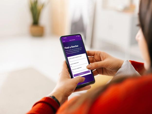 Photography of two hands holding their mobile phone, which displays the NYU Langone's Find-a-Doctor tool.