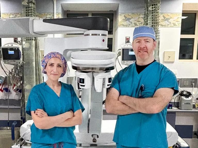 Dr. Martinez and Dr. Corcoran stand in front of robotic surgery equipment they use.