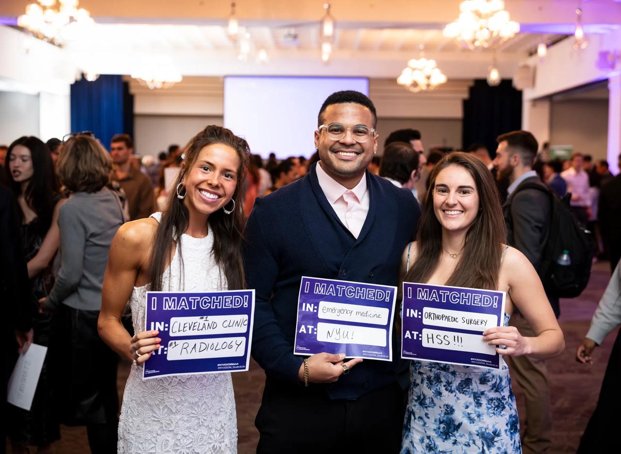 Three soon-to-graduate medical students from the Grossman School of Medicine smile and hold up pieces of paper that say "I Matched" in bold purple letters.