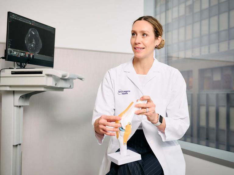 Abigail Campbell, MD, holds up an anatomical model while sitting in an exam room.
