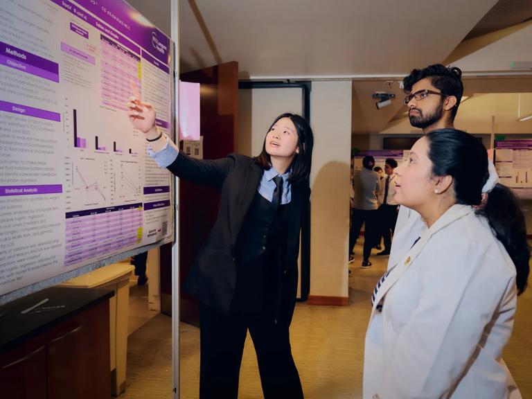 A female Grossman School of Medicine student presents her project to a woman and man during the school's Research Day.
