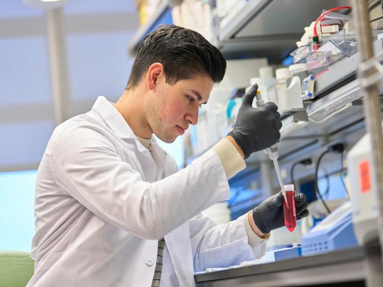 A male researcher stands in a lab while holding a vial.