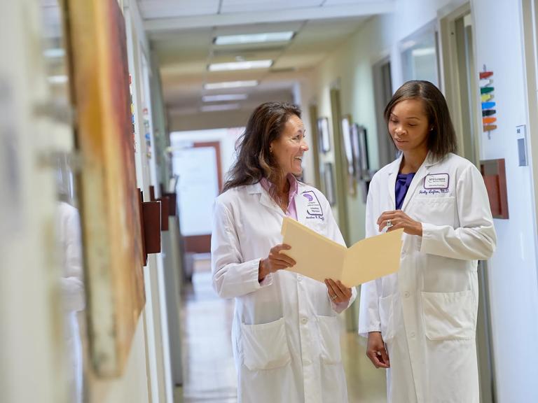 Holly F. Lofton, MD, right, and Christine J. Ren-Fielding, MD, left, stand next to each other looking at a folder in a hallway.