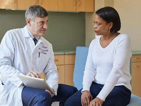 Mark Pochapin, MD, left, sits while speaking to a female patient, right, in an exam room.
