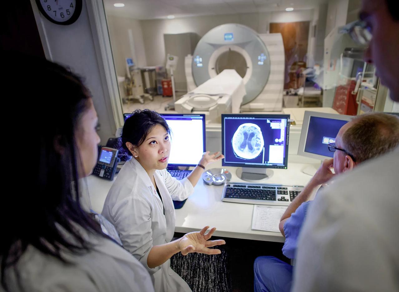 Koto Ishida, center left, with Michelle Gapay, left, and Jose Torres, standing at right, next to a brain scan on a computer screen.