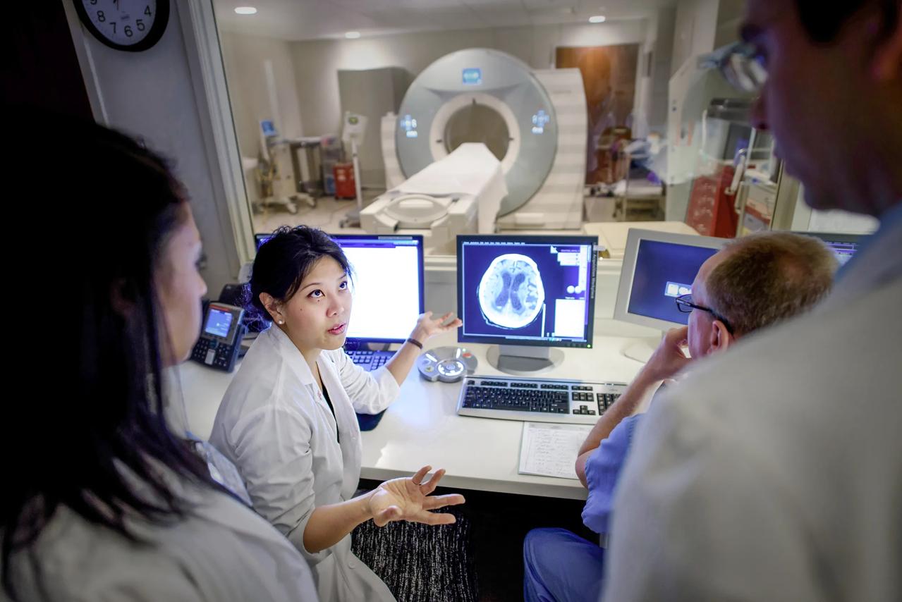 Koto Ishida, center left, with Michelle Gapay, left, and Jose Torres, standing at right, next to a brain scan on a computer screen.