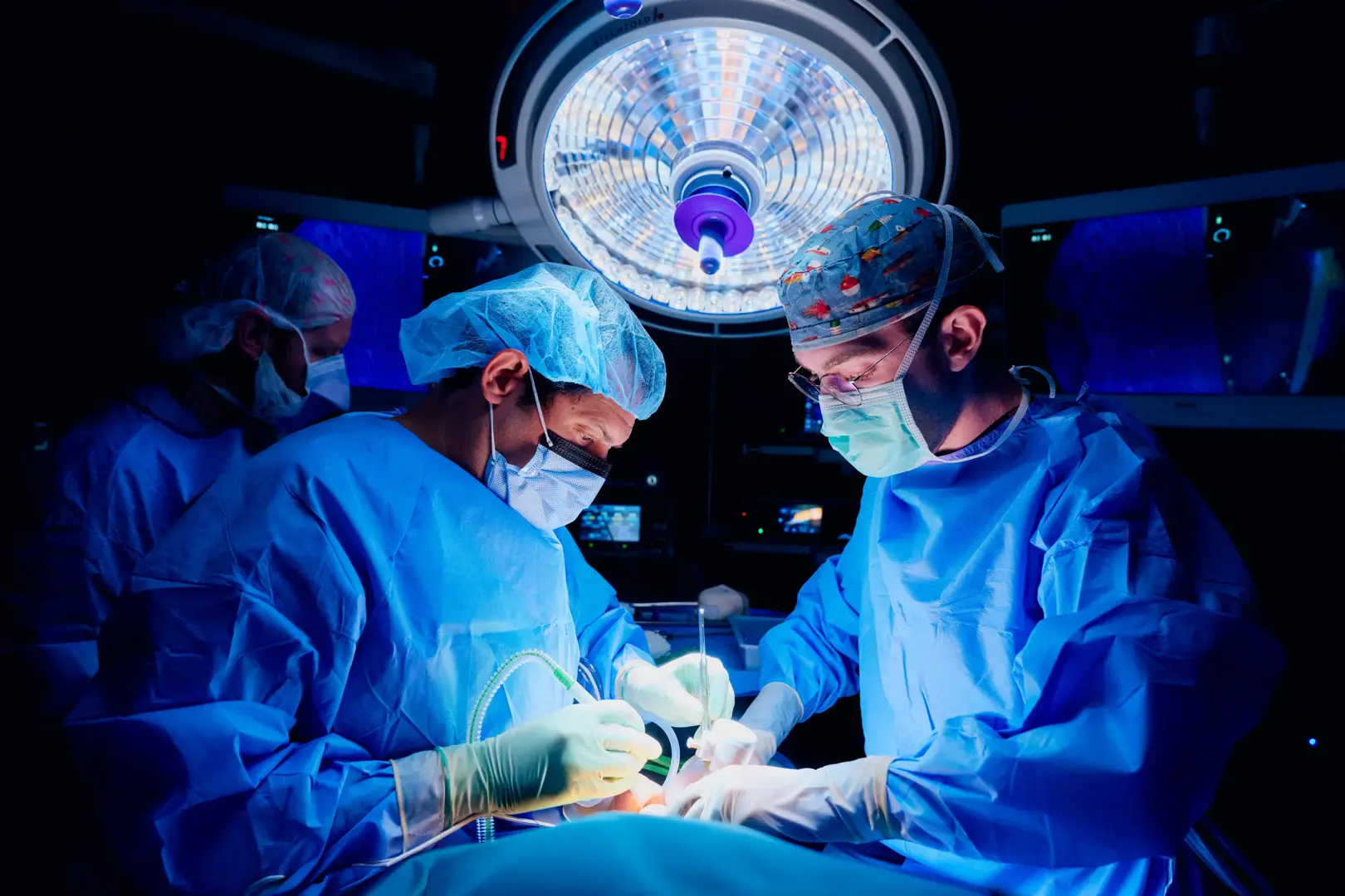 Bruce Gelb, MD, left, and a male doctor, right, wear scrubs and personal protective gear while performing a kidney transplant in an operating room.