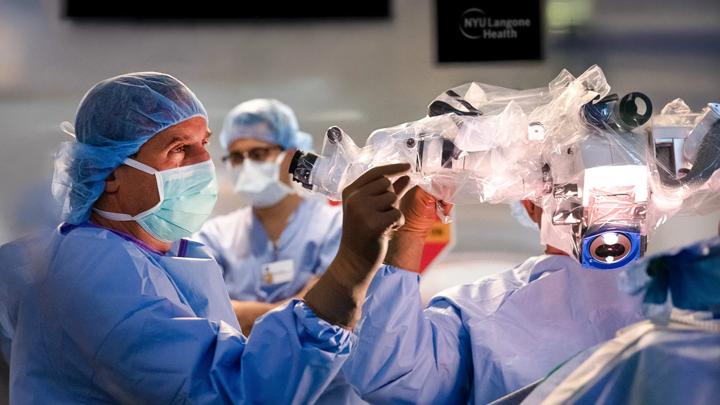 John Golfinos, MD, stands in front of an operating microscope in an operating room.
