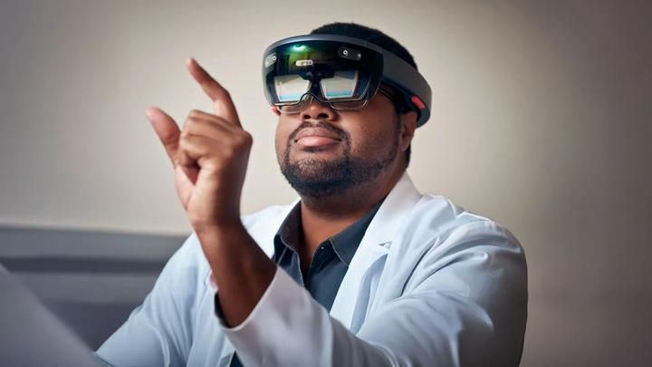 A man, seated, wears a virtual reality headset and holds up his hand.