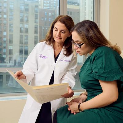 Mary Gemignani, MD, left, stands next to a female patient, right, seated, and holds a folder open. Together, they look down at the folder.