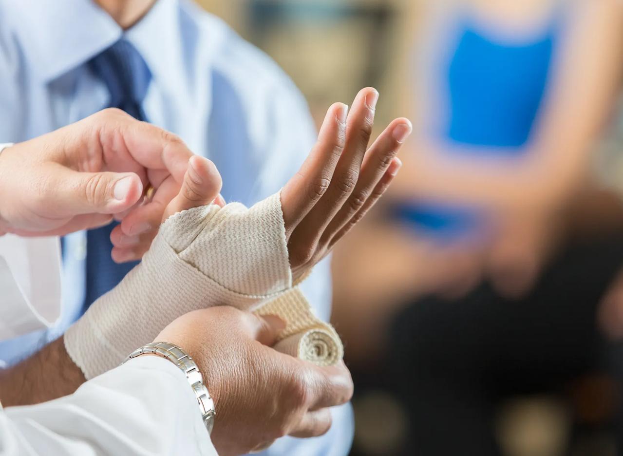 Photography of a hand being held and wrapped up in bandage by a medical professonal.