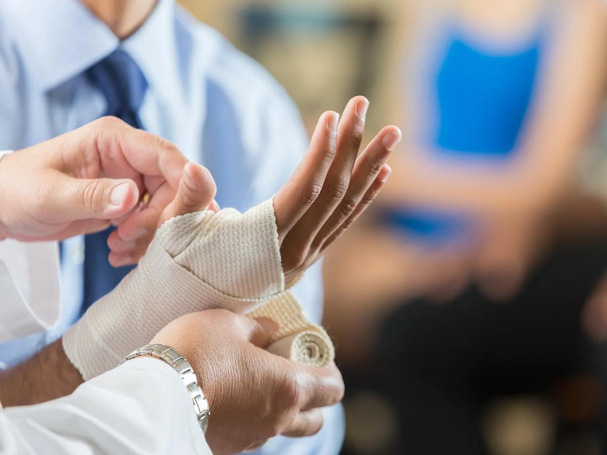 Photography of a hand being held and wrapped up in bandage by a medical professonal.