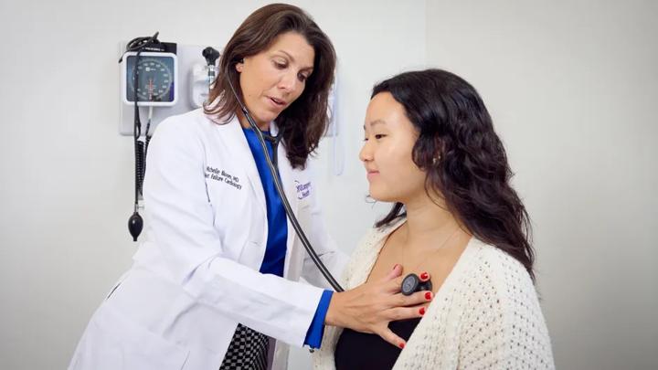 Michelle Bloom, MD, uses a stethoscope to listen to a seated patient&rsquo;s heart in an exam room.