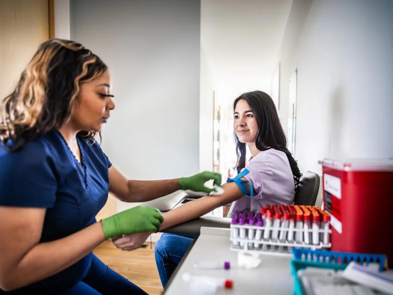 A phlebotomist prepares to draw blood from a young woman.