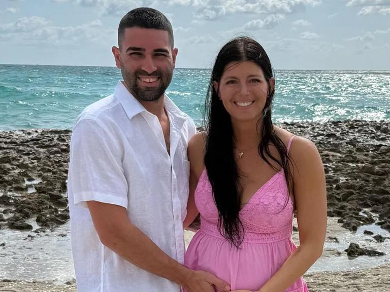 Christina and Jeremy standing and smiling in front of a beach.
