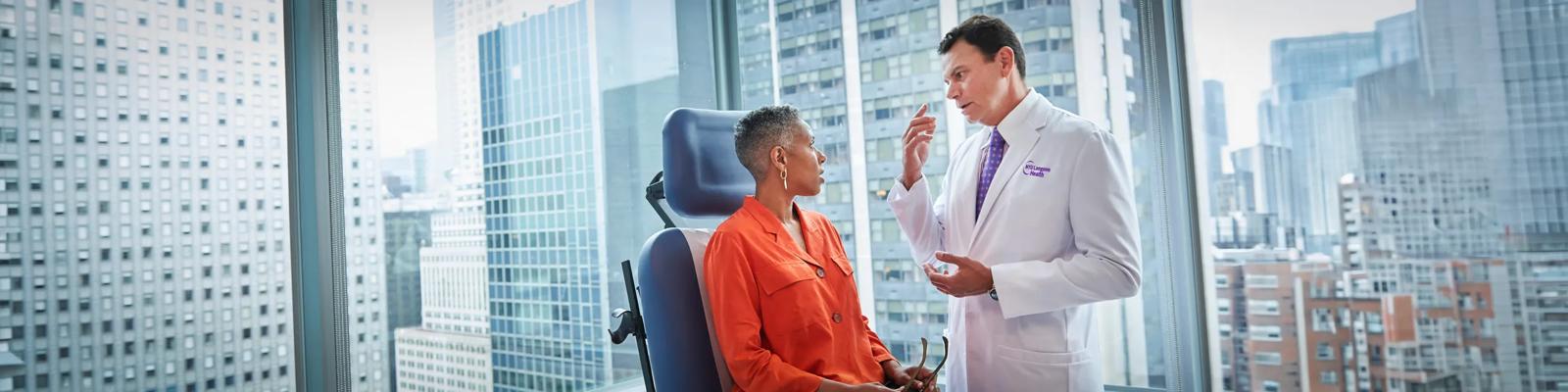 Rodrigo Eduardo, MD, right, stands next to a female patient who is sitting in an exam chair.