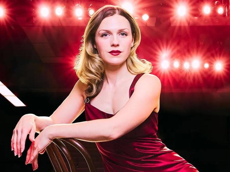 Caitlin Zerra Rose poses in a red dress in front of a black background.