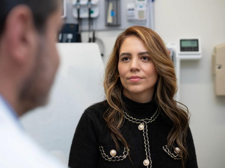 A female patient sits on an exam bed and looks in the direction of a doctor facing her.
