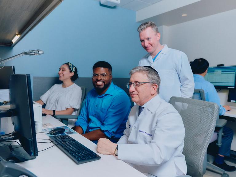 Michael Zelefsky, MD, right, sits next to two men and a woman in a computer lab looking at a monitor.